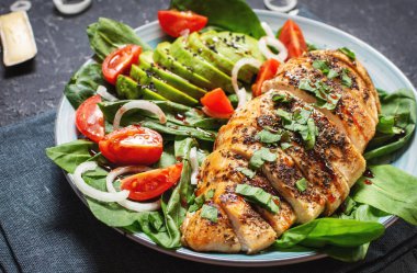 Izgara tavuk göğsü ve ıspanaklı avokado salatası ve siyah taş arka planda vişneli domates. Sağlıklı yemek, ketojenik diyet, öğle yemeği konsepti..
