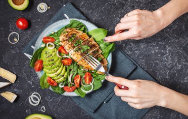 Izgara tavuk göğsü ve ıspanaklı avokado salatası ve siyah taş arka planda vişneli domates. Sağlıklı yiyecekler, ketojenik diyet, öğle yemeği konsepti. Üst görünüm