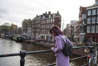 Paltolu ve sırt çantalı kız şehrin tadını çıkarıyor. Hollanda, Avrupa 'da Amsterdam kanalının kenarına bakan genç bir kadın.
