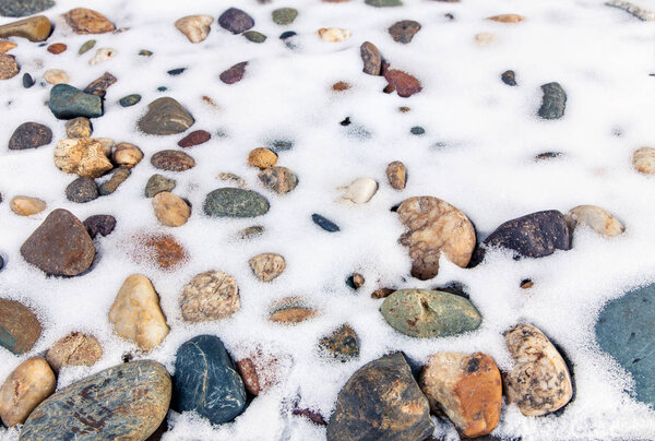 Snow lies on a stone shore. Background of stones and fresh snow