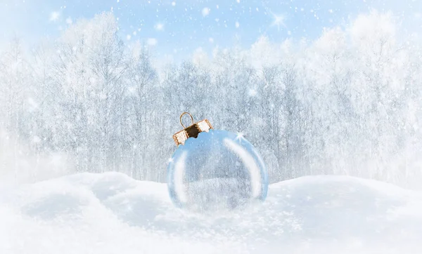 Bir kış ormanının arka planında, karda şeffaf bir Noel topu..