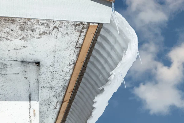 Binanın çatısından mavi gökyüzünün arka planına doğru tehlikeli kar ve buz düşüşü. Bahar Buzu