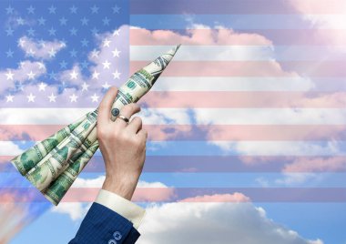 Doların büyümesi kavramı. Bulutlu mavi gökyüzüne ve Amerikan bayrağına karşı bir iş adamının elinde bir roket dolusu para. Başarılı bir iş. Döviz bürosu. Ticaret ve yatırım.