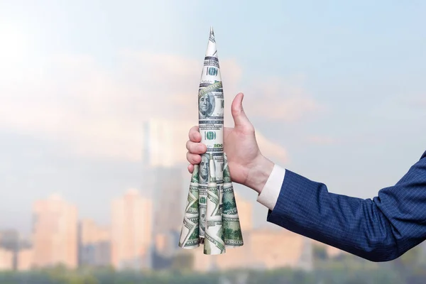 İş adamının elinde şehrin arka planına karşı bir dolarlık bir roket var. Jesti işaret ediyor. Amerikan para birimi büyüme kavramı