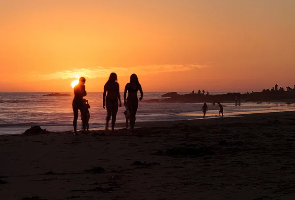 Sylwetki osób korzystających z plaży o zachodzie słońca — Zdjęcie stockowe