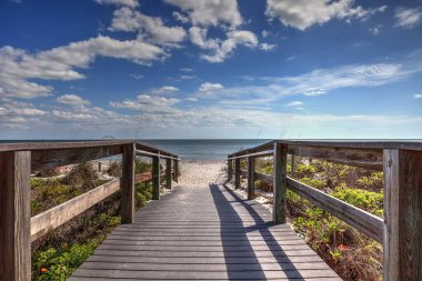 Boardwalk leading to Lighthouse Beach Park in Sanibel, Florida under a blue sky. clipart