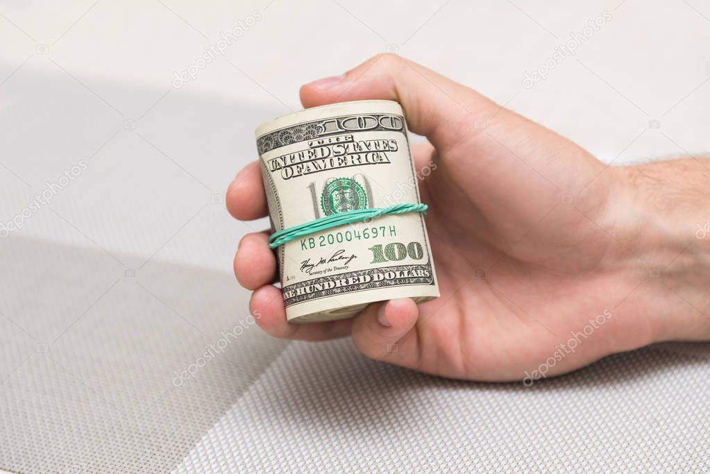 A man holds a bundle of money in his hand tied with an elastic band