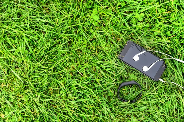 Phone and headphones on green grass — Stock Photo, Image