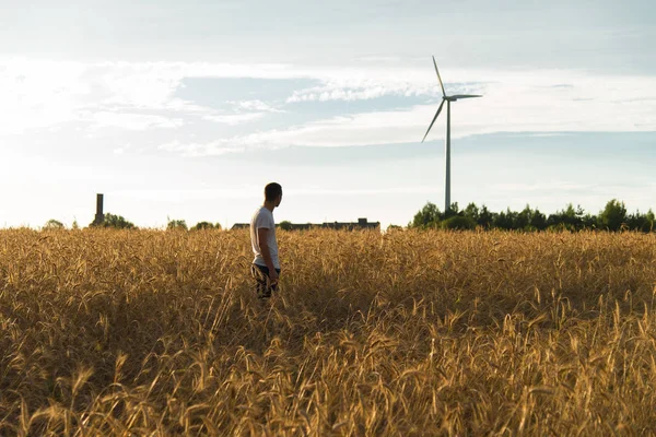 Человек, стоящий в поле и смотрящий на ветрогенератор — стоковое фото