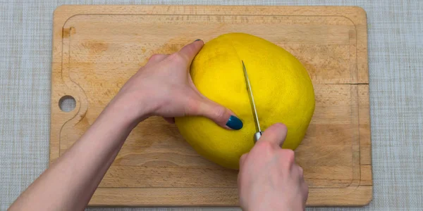 Girl cleans a pomelo on a wooden board — Stock Photo, Image