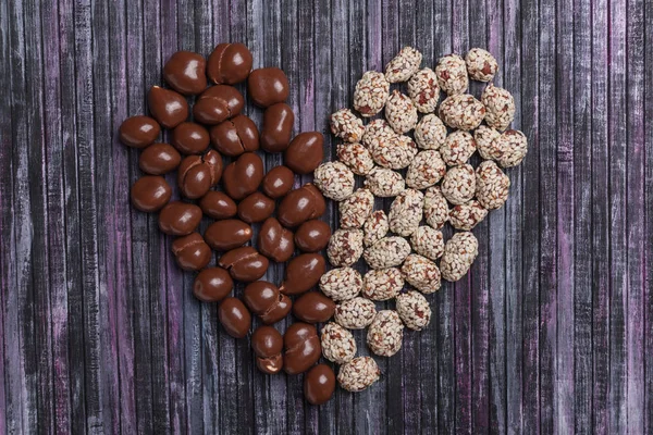 Peanuts in chocolate. Peanut with caramel and sesame seeds. Sweet peanut posted heart.