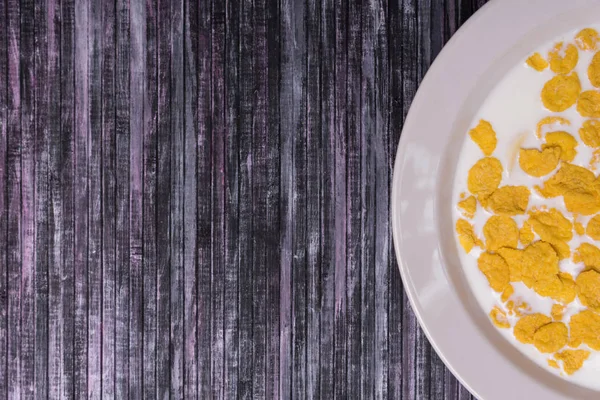 Corn flakes with milk. Plate on a wooden background. White dish with flakes. Yellow flakes. Salvage is a waste.