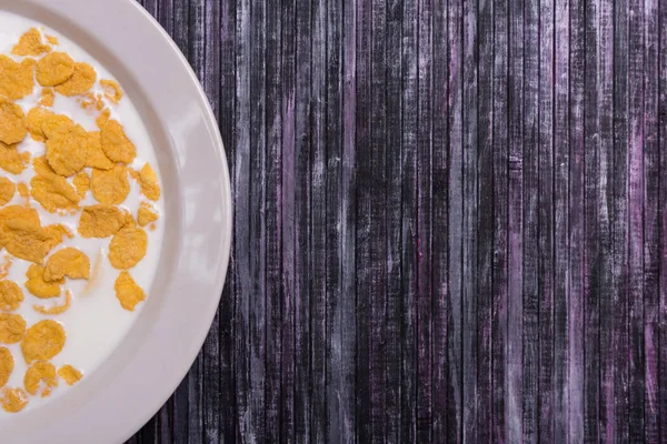 Corn flakes with milk. Plate on a wooden background. White dish with flakes. Yellow flakes. Salvage is a waste. — Stock Photo, Image