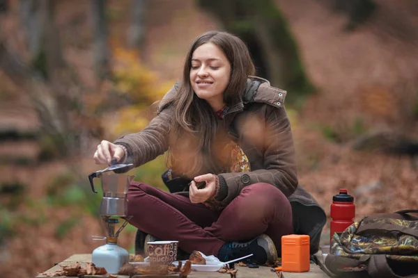 Young female woman making coffee in aluminium coffee maker outdoors in autumn forest