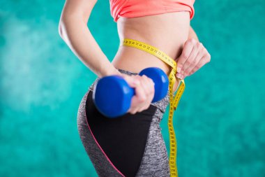 Spor fitness kızla dumbell ve tape ölçmek için diyet - turkuaz arka plan üzerinde izole. Tatlılar sağlıksız. Abur cubur. Diyet, sağlıklı beslenme.