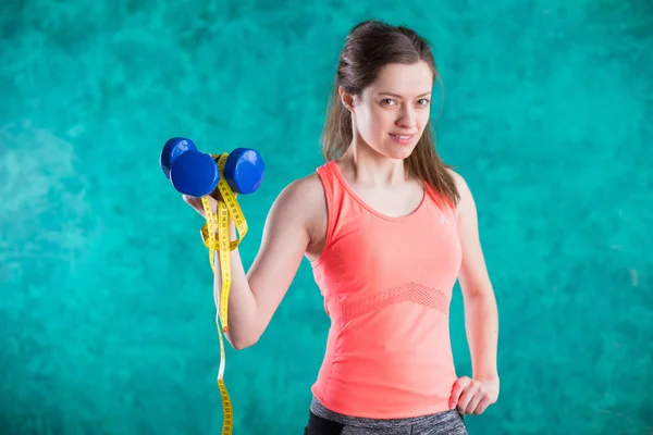 Sport fitness girl with dumbbells and tape measure for diet  - isolated on the turquoise  background.Sweets are unhealthy. Junk Food. Dieting, Healthy Eating.