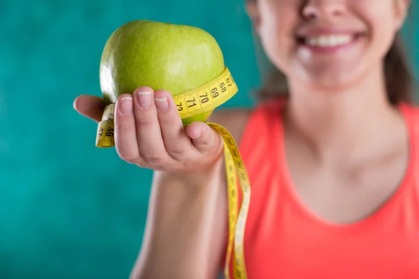Diet. Healthy happy female with apple and tape measure for diet and weight loss concept - isolated on the turquoise  background. Sweets are unhealthy. Junk Food.