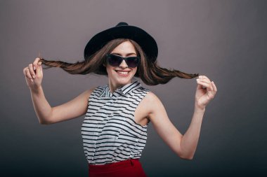 Güzel moda olan kadın siyah şapka ve gözlük gri arka plan üzerinde moda makyaj. Modeli şık gözlük takıyor kameraya bakıyor. Kadın moda, güzellik kavramı. 