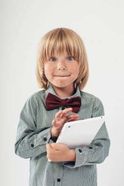 Tablet bilgisayar beyaz arka planda tutan gülümseyen okullu çocuk gömlek ile kırmızı papyon,
