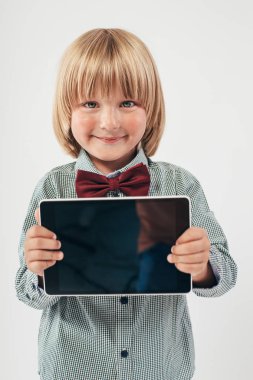 Tablet bilgisayar beyaz arka planda tutan gülümseyen okullu çocuk gömlek ile kırmızı papyon,