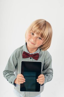 Tablet bilgisayar beyaz arka planda tutan gülümseyen okullu çocuk gömlek ile kırmızı papyon,