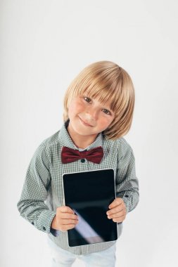 Tablet bilgisayar beyaz arka planda tutan gülümseyen okullu çocuk gömlek ile kırmızı papyon,