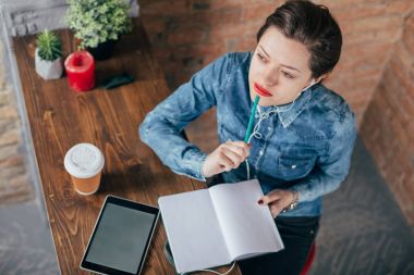 Not defteri ve tablet ile güzel genç kadın serbest meslek çatı iç odasında bir kahve molası var