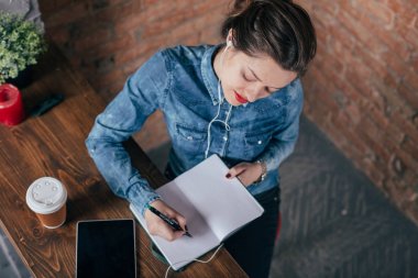 Not defteri ve tablet ile güzel genç kadın serbest meslek çatı iç odasında bir kahve molası var