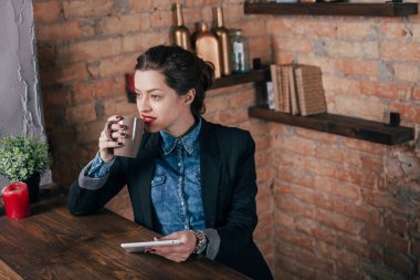 Not defteri ve tablet ile güzel genç kadın serbest meslek çatı iç odasında bir kahve molası var