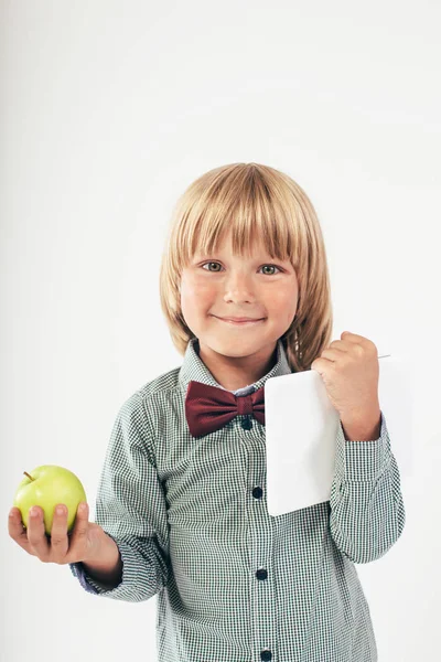 赤い蝶ネクタイ付きシャツ ホワイト バック グラウンドでタブレット コンピューターと青リンゴを保持している児童の笑顔 — ストック写真