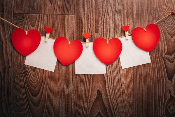 Love Valentine's hearts and card natural cord and red clips hanging on rustic driftwood texture background, copy space