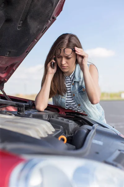 Girl near a broken car on the country road is calling on mobile phone.