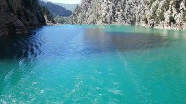 Oimapinar Barajı 'nın çevresindeki dağ kayalıkları arasında bir gölde seyreden bir tekne görüntüsü. Yeşil Kanyon, Manavgat, Antalya, Türkiye
