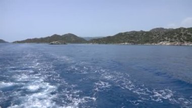 Seyir gemisinin izini sakin denizle sürün. Kekova adası yakınlarındaki Türk kayalık kıyılarının manzarası. Yavaş çekim