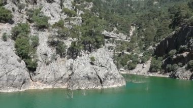 Oimapinar Barajı 'nın çevresindeki dağ kayalıkları arasında bir gölde seyreden bir tekne görüntüsü. Yeşil Kanyon, Manavgat, Antalya, Türkiye