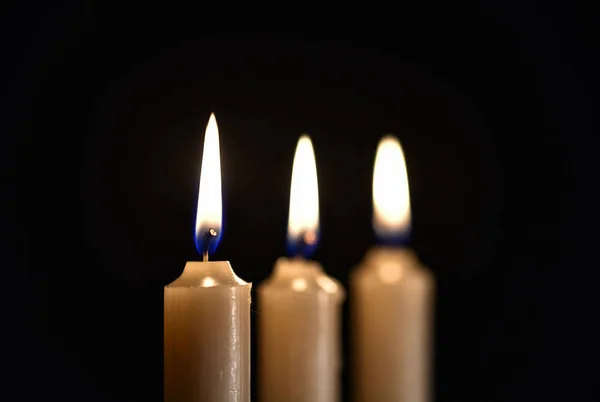 Three burning wax candles on a black background