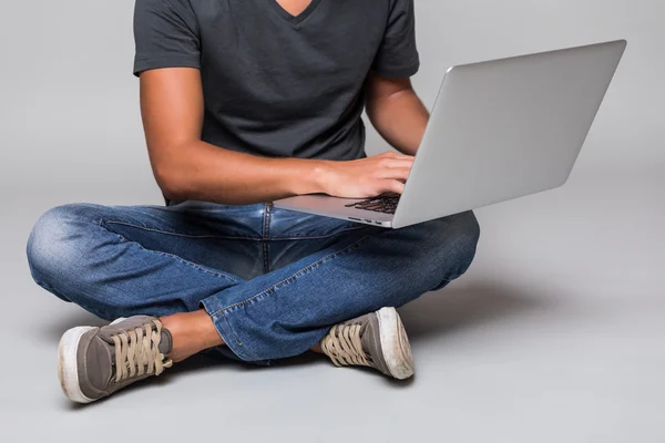 Imagen recortada de un feliz hombre casual sonriente sentado en el suelo con el ordenador portátil — Foto de Stock