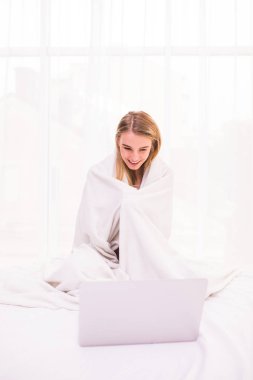 Yatak yorgan altında yatan ve dizüstü bilgisayar kullanarak çekici genç kadın