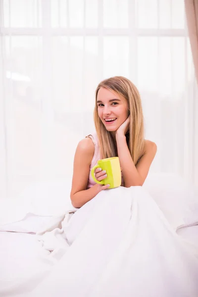 ベッドでコーヒーを飲みながら美しい若い女性の肖像画. — ストック写真