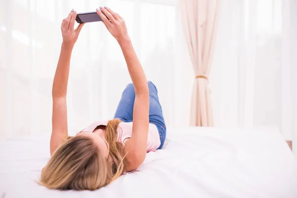 Красивая блондинка отправляет смс на кровать в спальне — стоковое фото