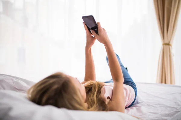 Pretty blonde girl sending a text on bed at home in the bedroom — Stock Photo, Image