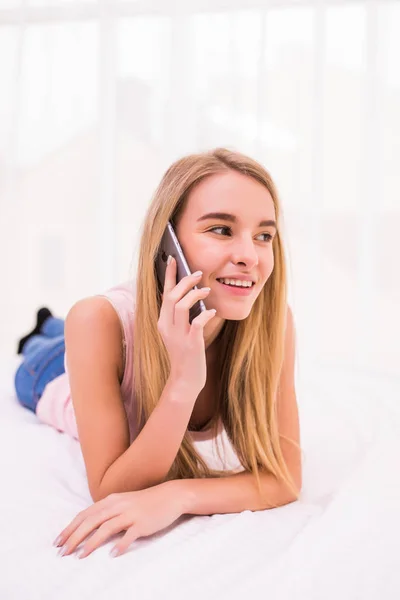 Ung blond tjej talar telefon i sin säng hemma — Stockfoto