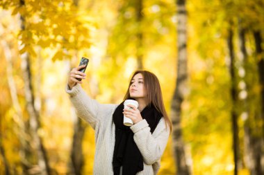 Genç kız al selfie fincan kahve ile telefonda sarı güneşli park