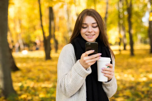 Улыбающаяся девушка делает селфи на мобильном телефоне в солнечном осеннем парке — стоковое фото
