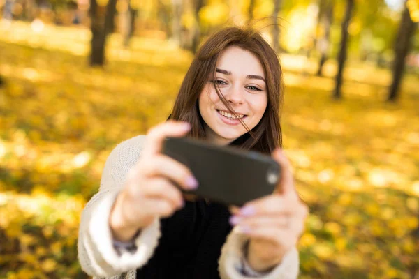 Smile girl taking selfie on mobile phone in sunny autumn park — Stock Photo, Image