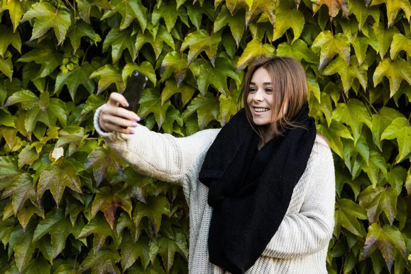 젊은 미소 녹색 잎 배경에 전화에 여자 걸릴 selfie — 스톡 사진