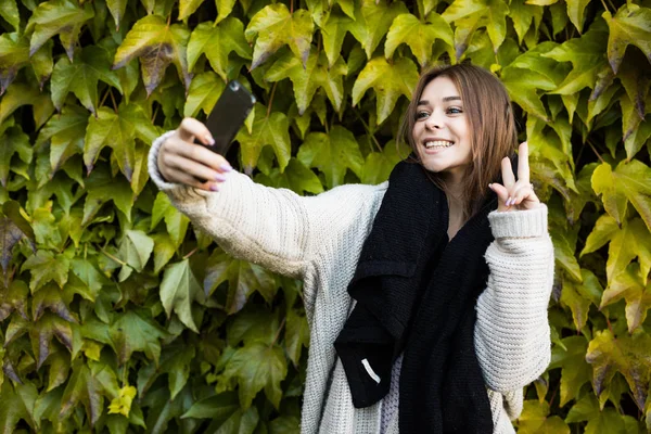 若い緑の葉の背景に携帯電話で女の子を取る selfie を笑顔します。 — ストック写真