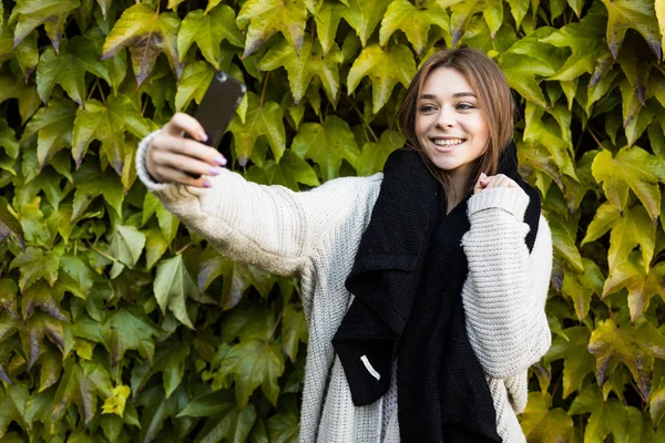 Joven sonrisa chica tomar selfie en el teléfono en verde hojas fondo — Foto de Stock