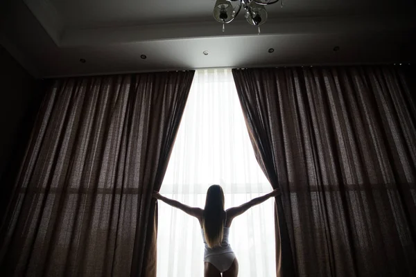 Girl is opening curtains and meeting sunrise — Stock Photo, Image