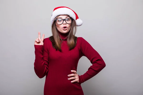 Verlaten kerst meisje met santa hat vinger omhoog op grijze achtergrond — Stockfoto